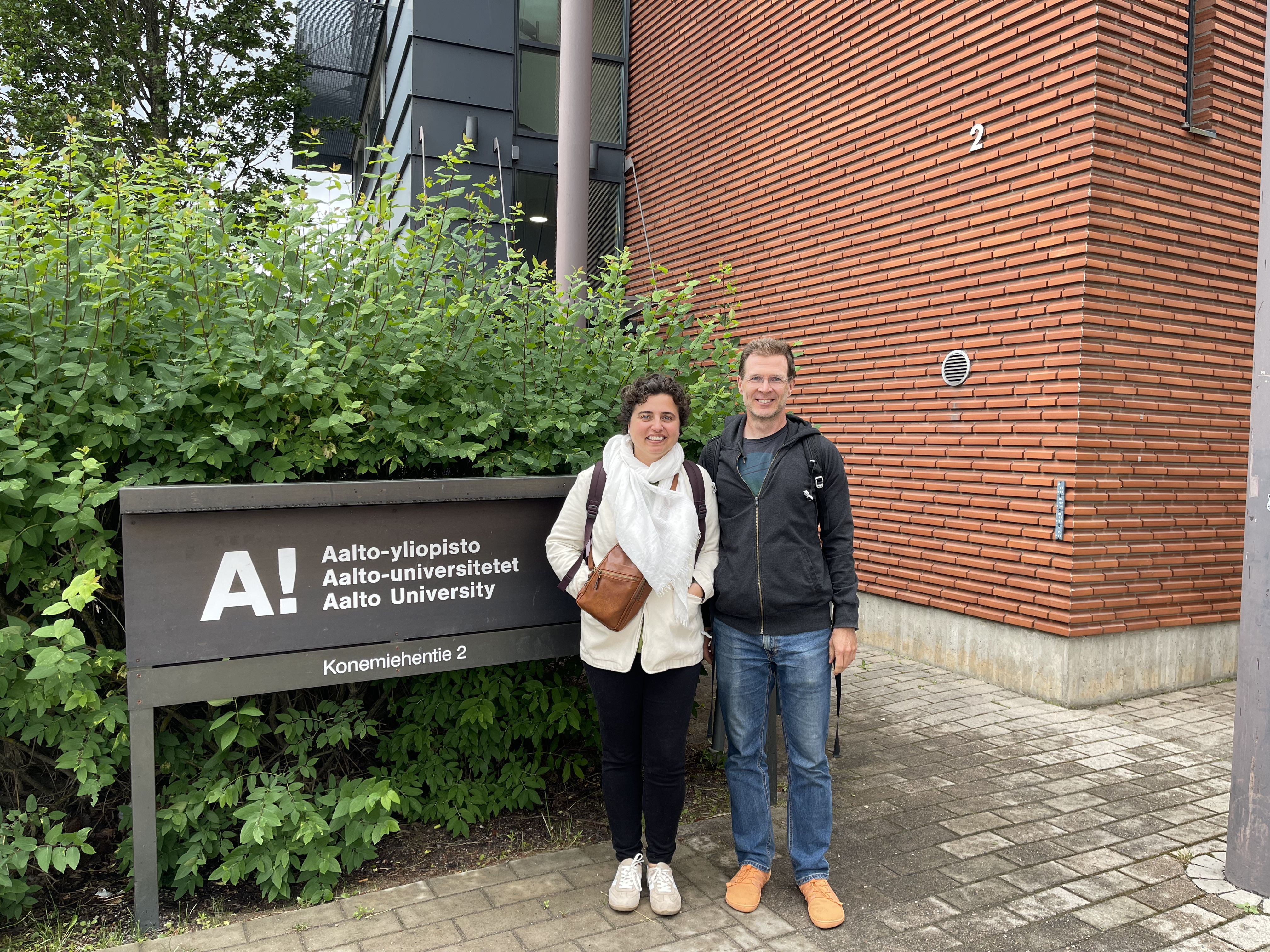 A man and a woman next to a sign that reads Aalto University with university's name written first in Finnish, then in Swedish, and then in English.
